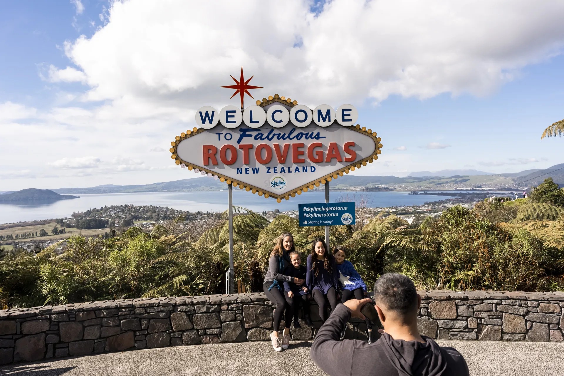 Person taking photo of a family under a sign reading "Welcome to Fabulous Rotovegas New Zealand".