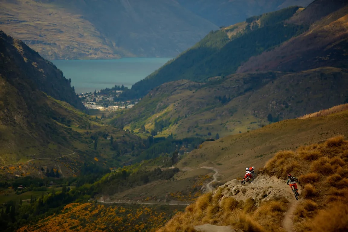 Two bikers cycling down a rocky path towards Queenstown.