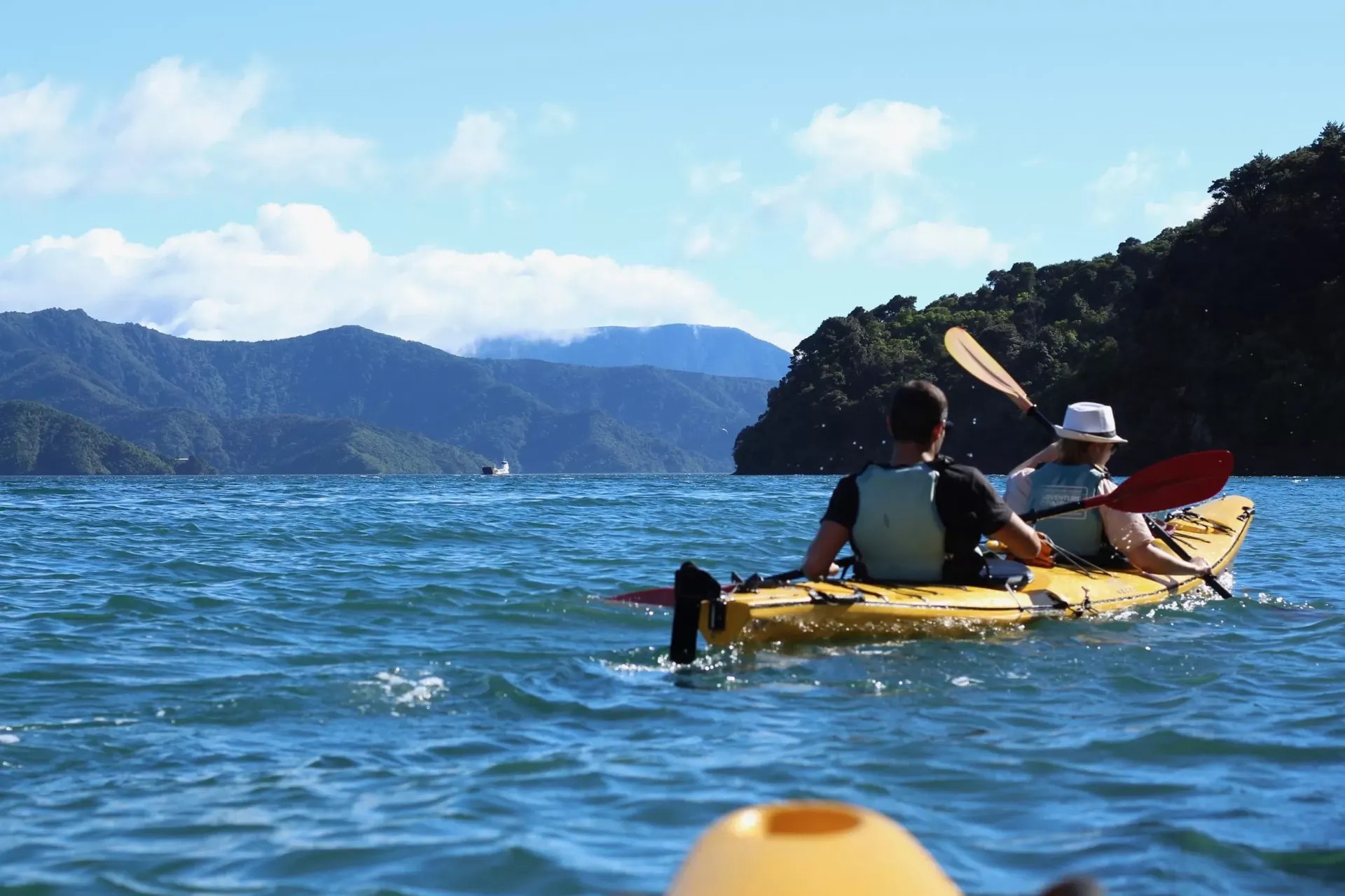 Two people paddling in a kayak between high cliffs.