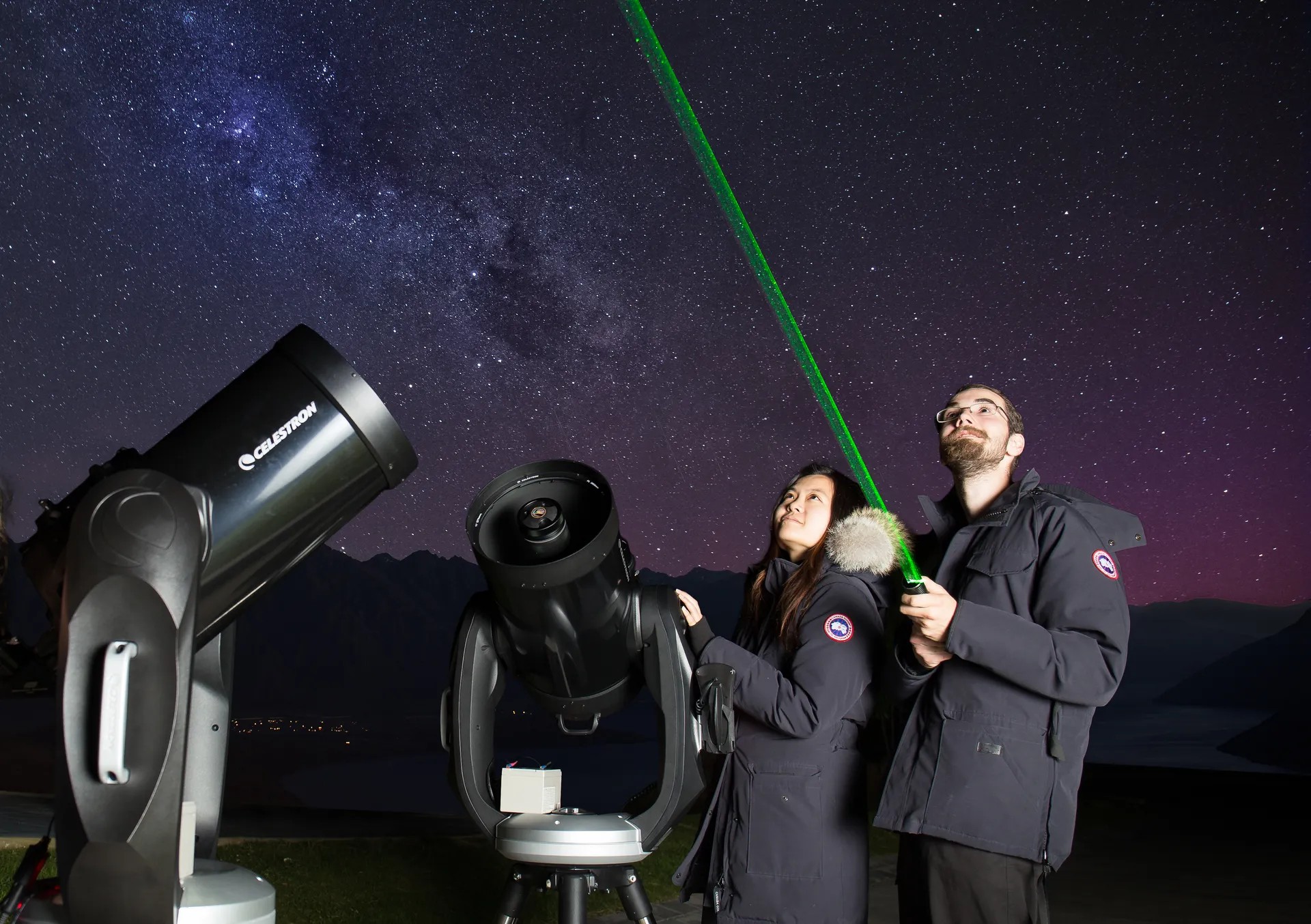 Couple looking at starry sky, pointing a green laser upwards.