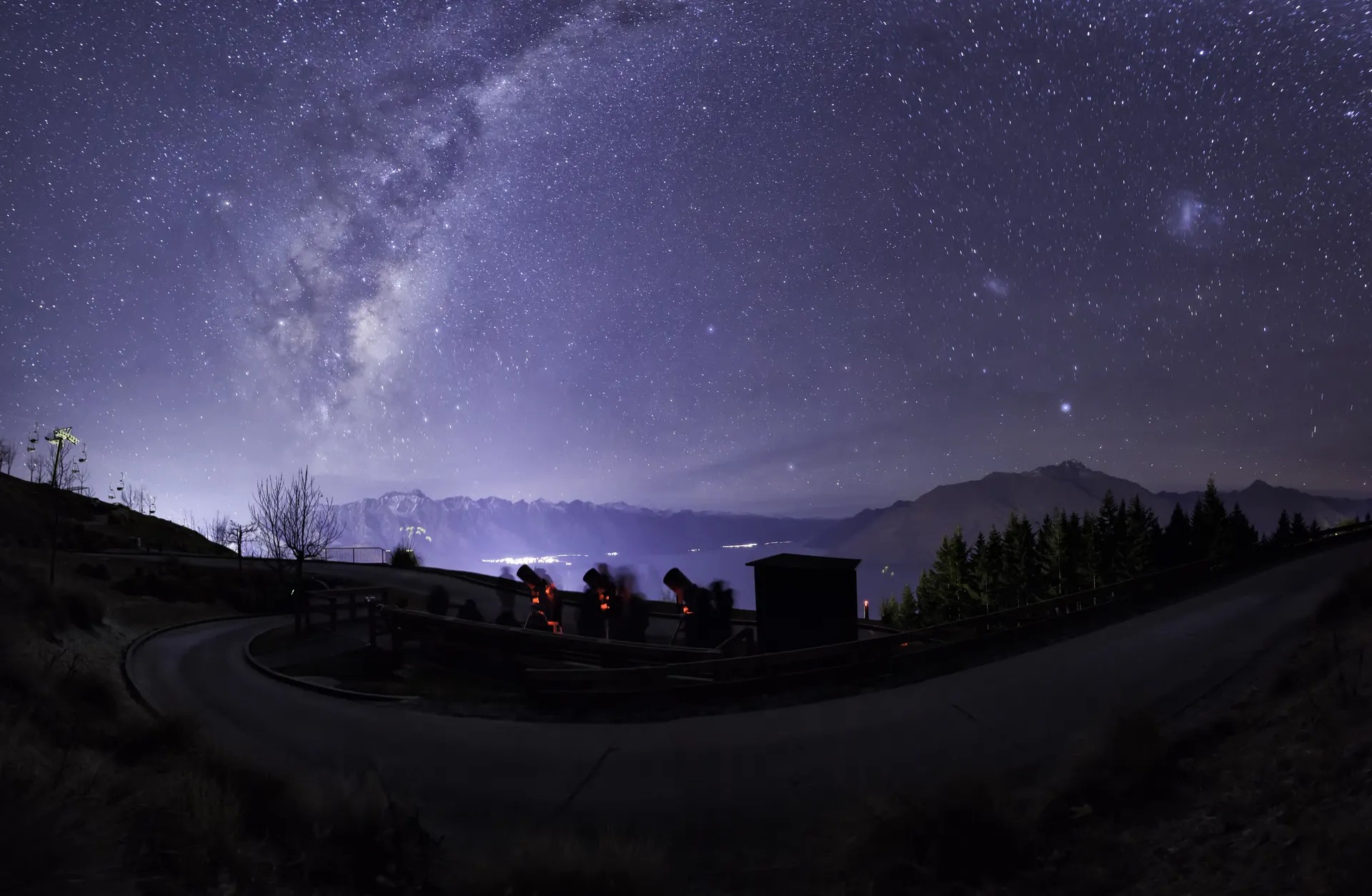 Starry night sky above Queenstown with the red glow of three telescopes in use.