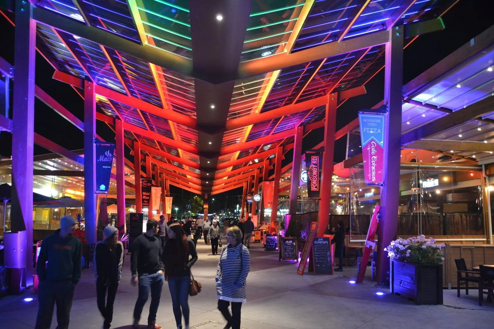 Street with a lit-up walkway cover and restaurants on each side of the path.