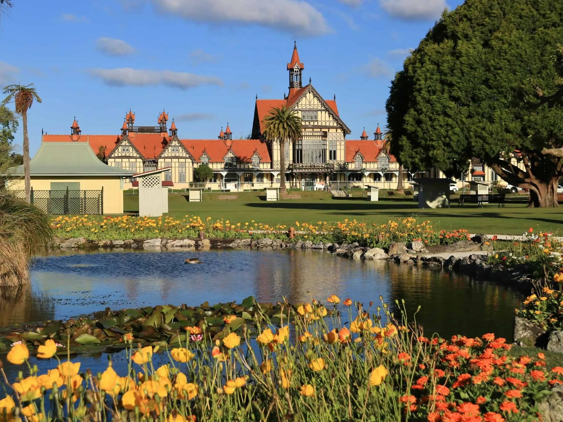 Old building in a park with a pond and flowers.