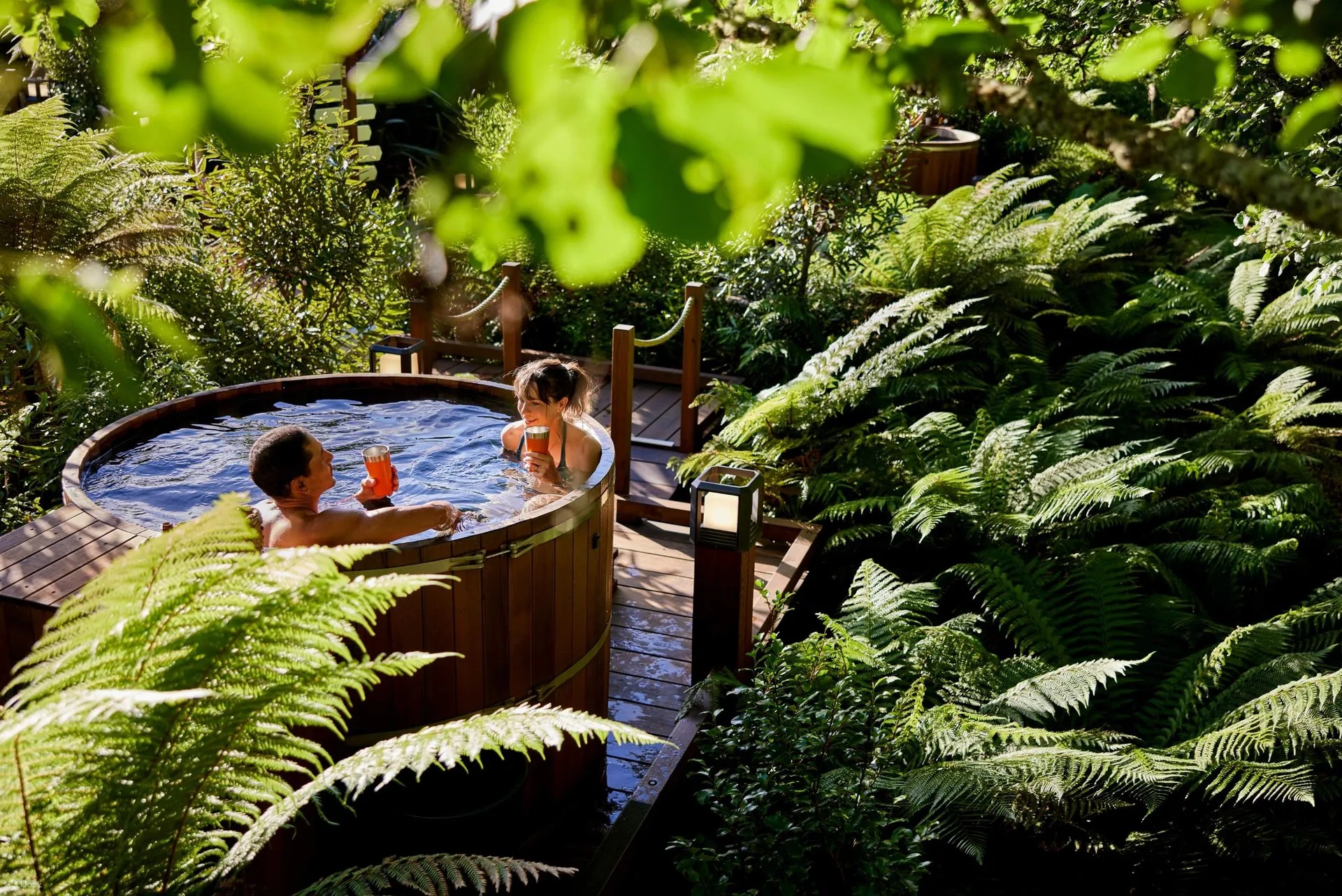 Couple drinking in a round cedar hot tub in a forest.
