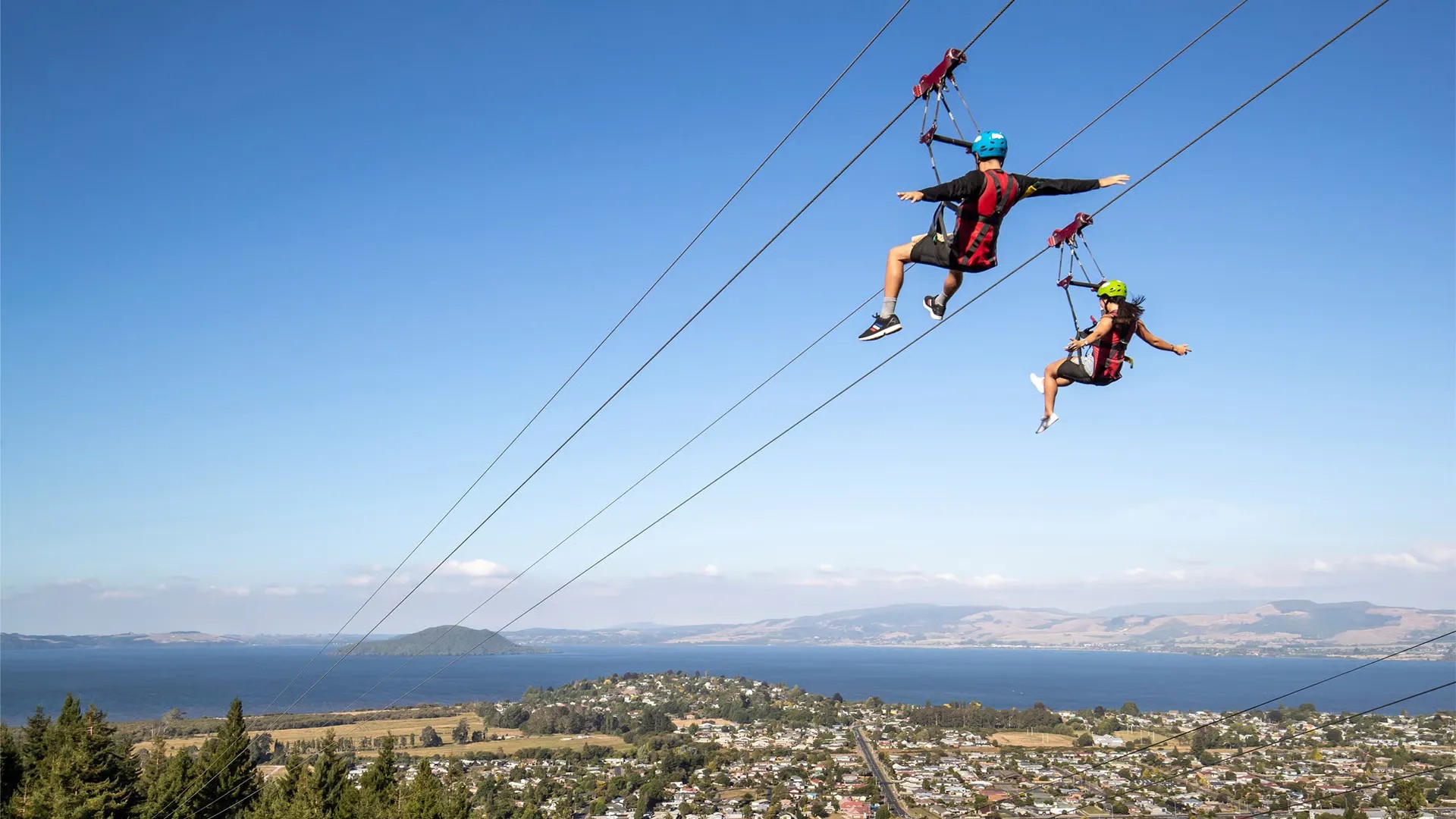 Two people riding on a zipline overlooking Lake Rotorua.