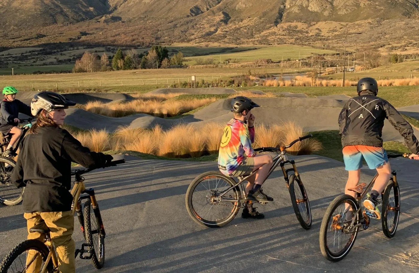 Young bikers idling on a bumpy concrete pump track by a mountain.