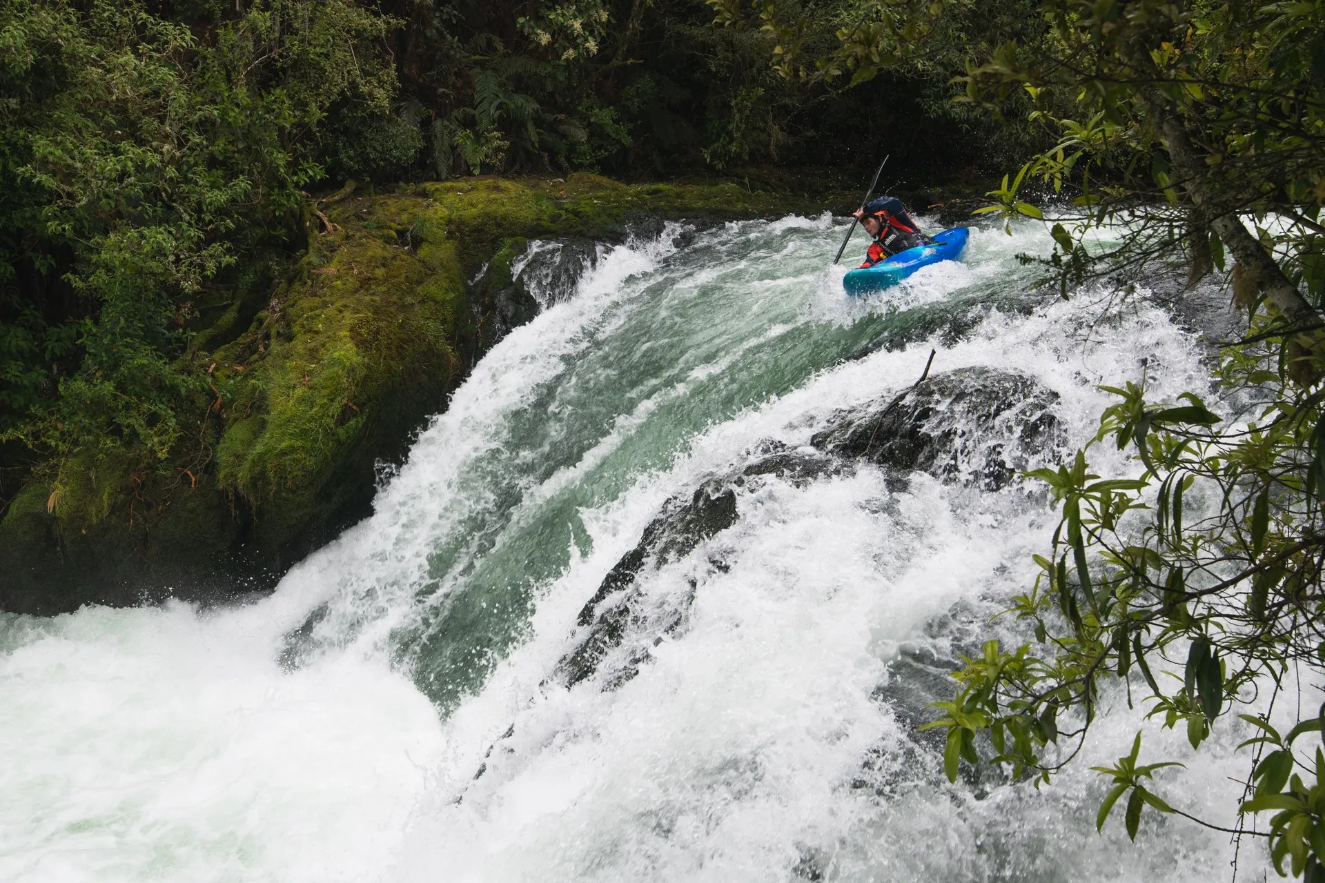 Person kayaking down a small waterfall.