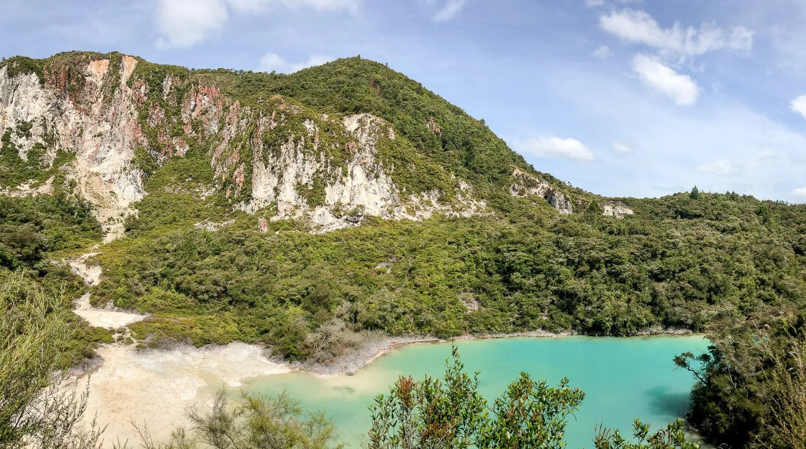 Turquoise lake below a lush, green, forested mountain.