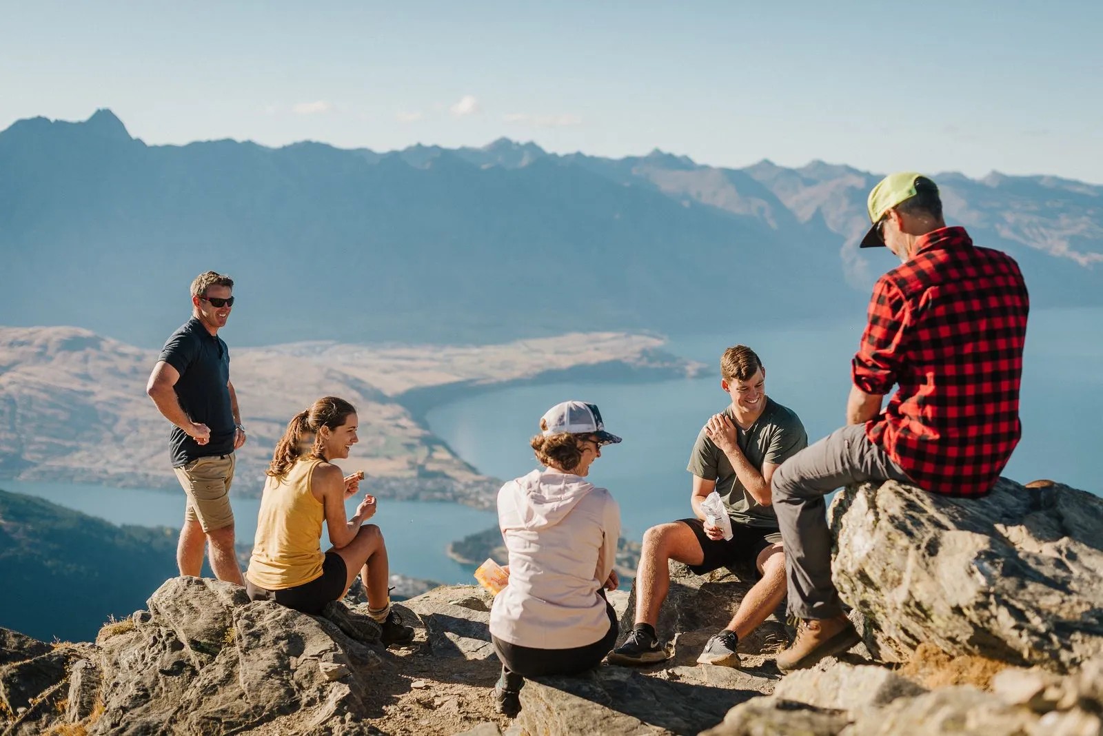 Group of people eating lunch on top of rocks on a mountain above the Wakatipu basin.
