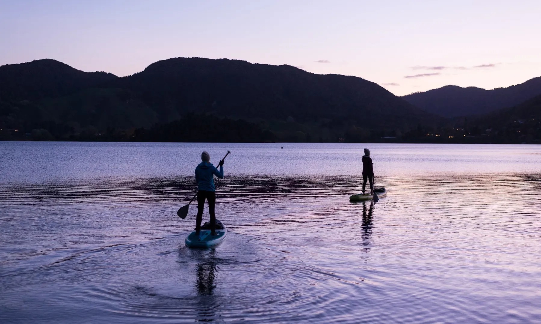 Two people paddleboarding on a lake at sunset.