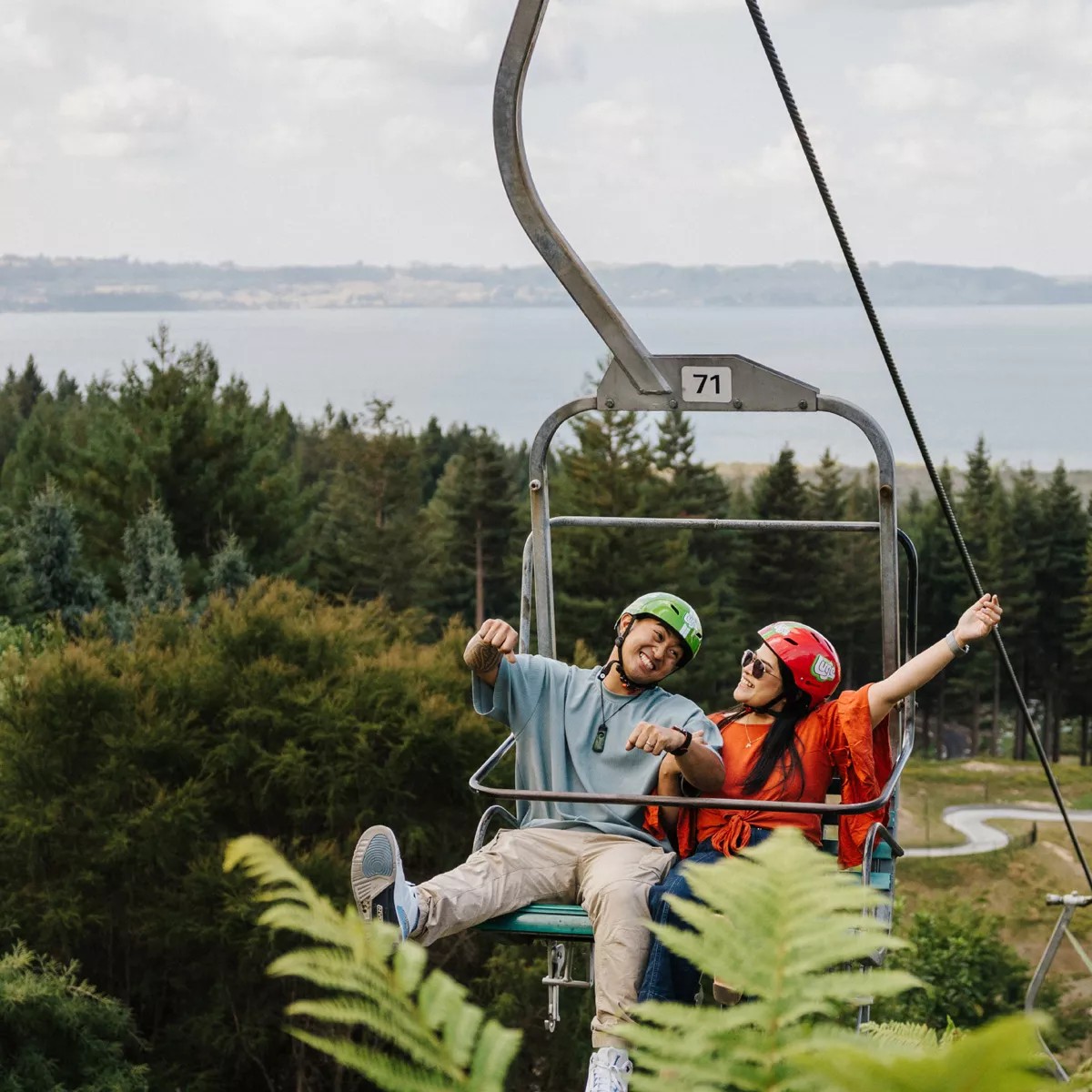 A young couple rides the Luge chairlift at Skyline Rotorua and poses for a photo.