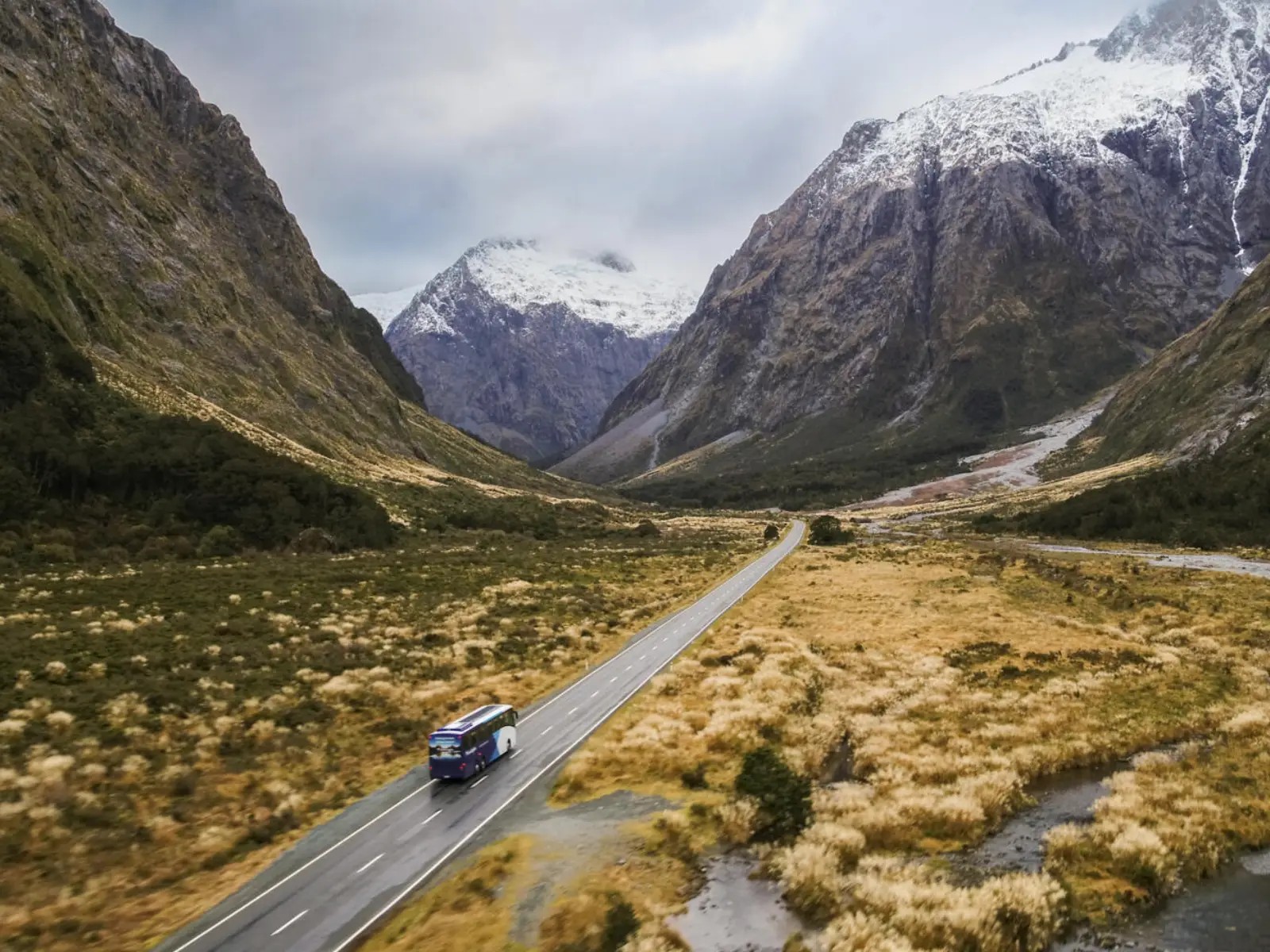 Coach travelling along the Milford Road through Fiordland National Park, surrounded by alpine valleys, rivers and snow-capped mountains in New Zealand