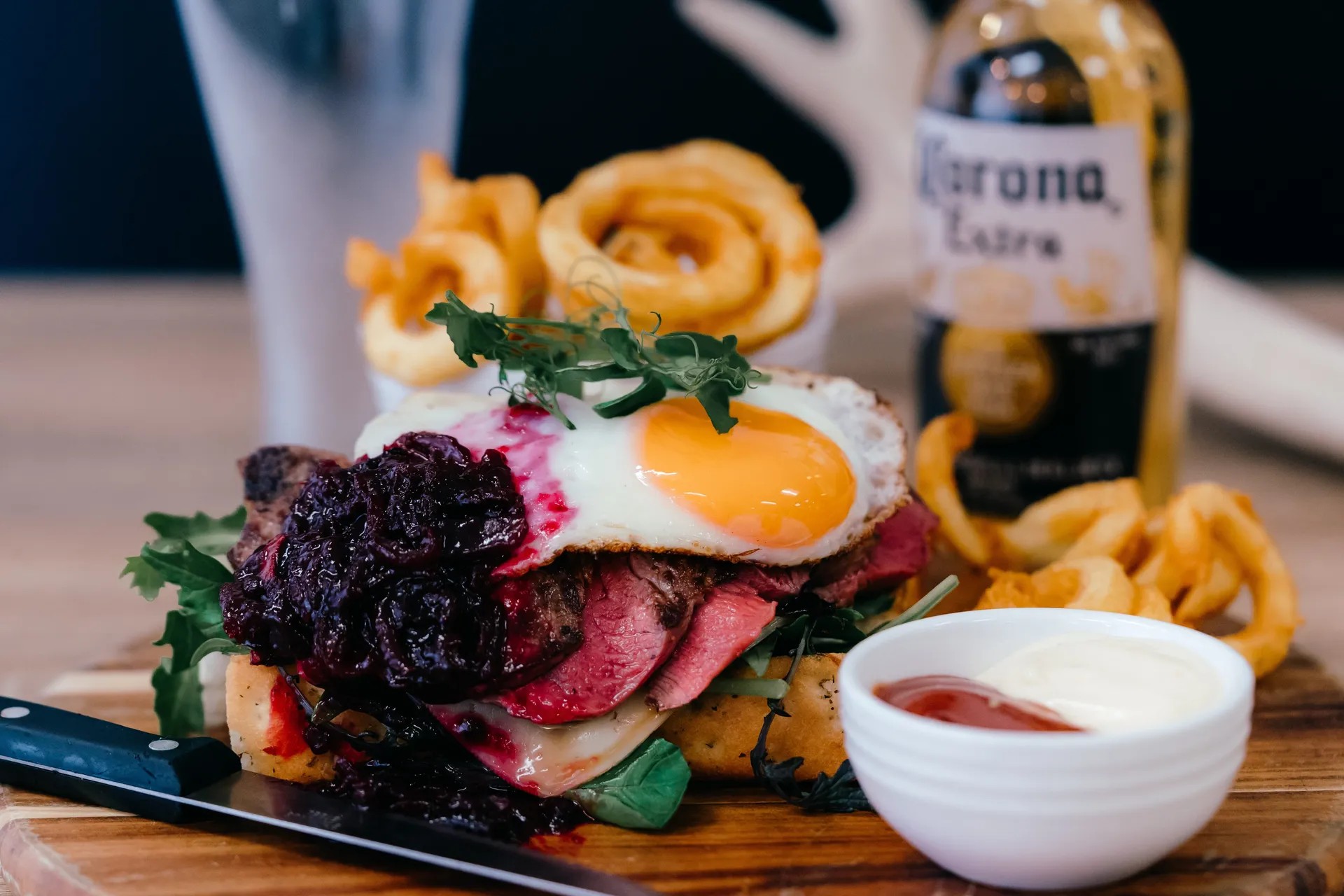Dish of steak and egg on bread, served with curly fries, sauce, and beer.
