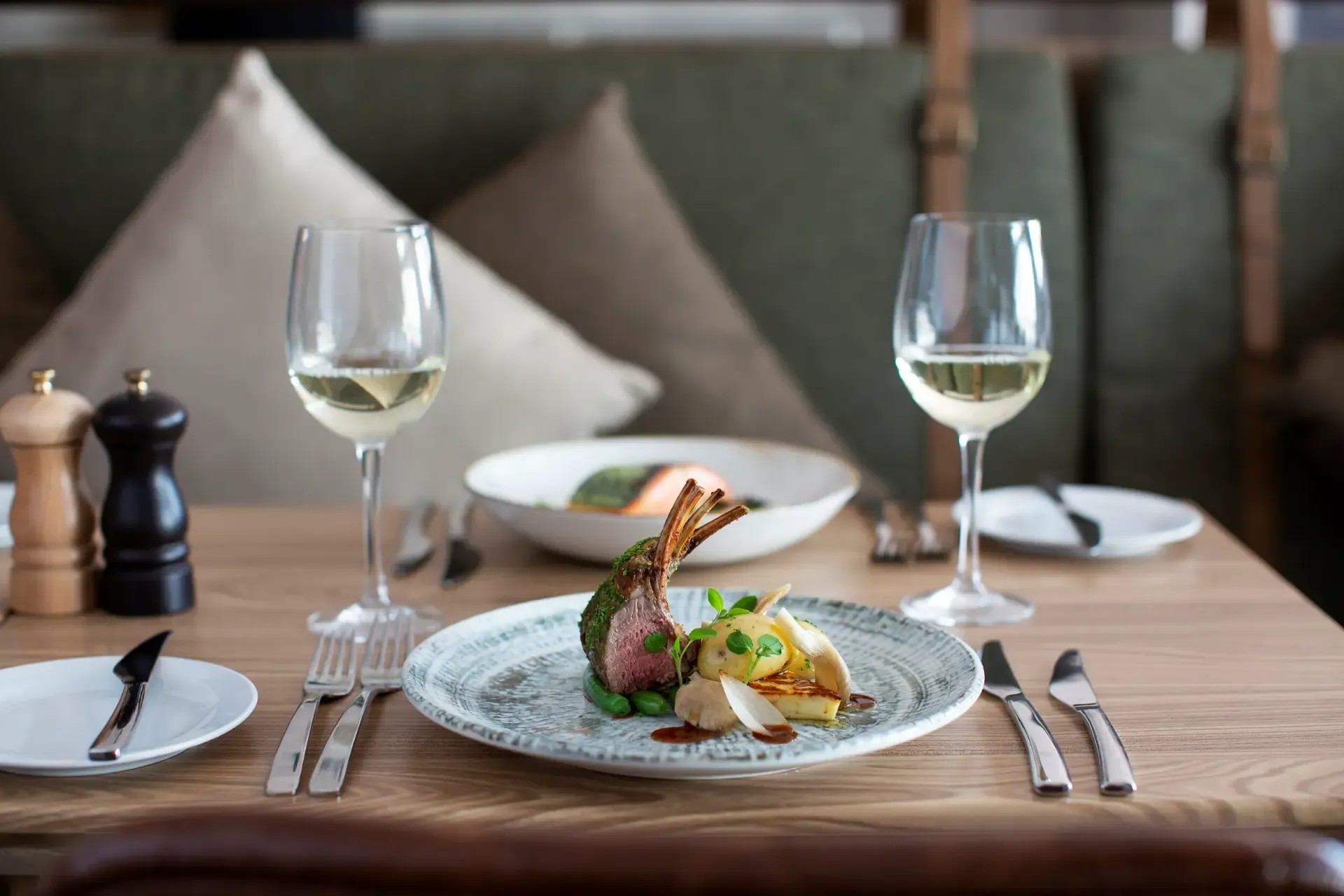 Lamb chops and potatoes accompanied by white wine in an elegant restaurant setting.