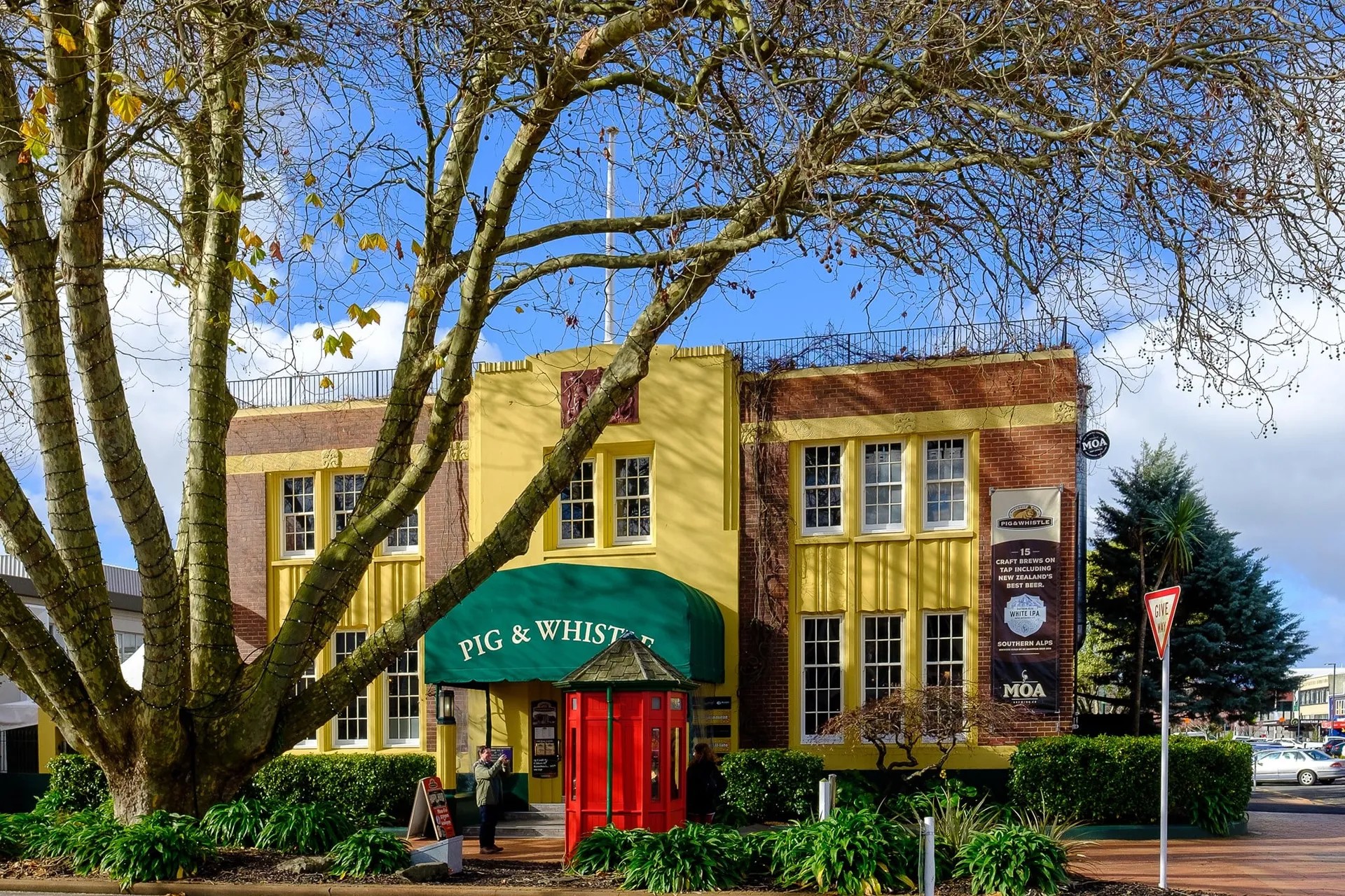 Pub set in a 1940's brick building partially painted yelow, with a red phone box and large tree in front.