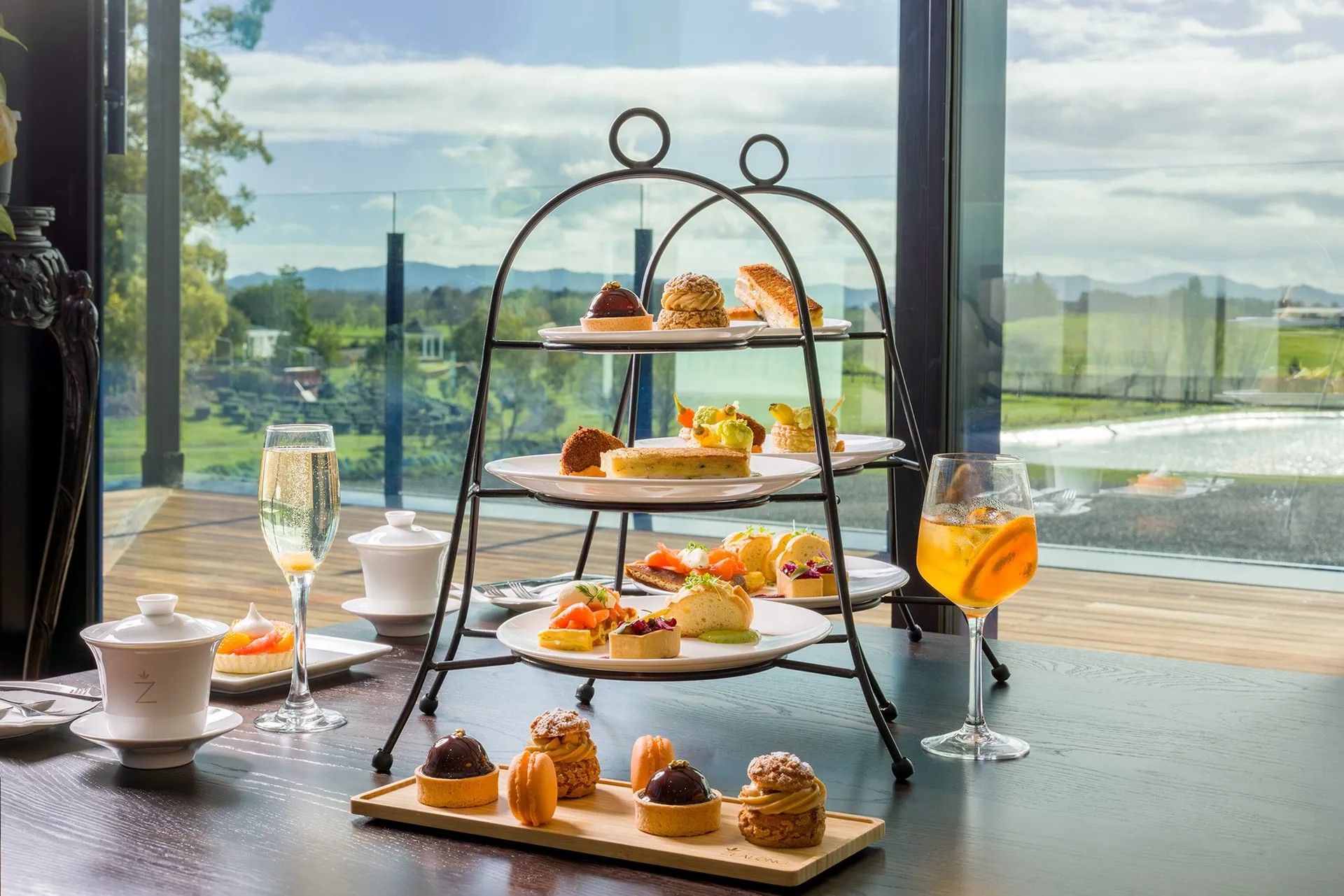 High tea setup with macarons, cake, and pastries. On the side are some tea and alcoholic drinks.