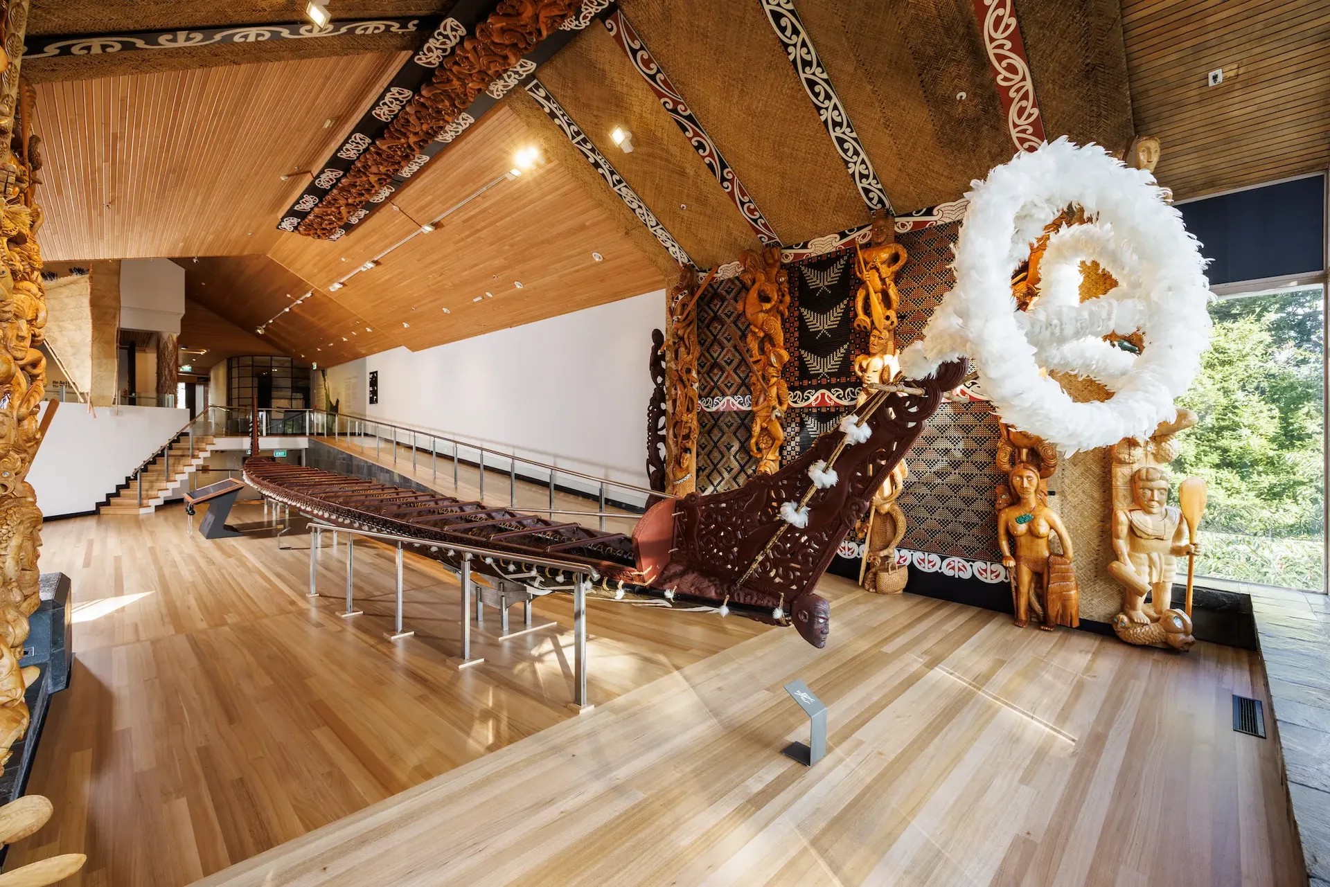 Large wooden waka war canoe inside a museum, surrounded by Maori carvings.