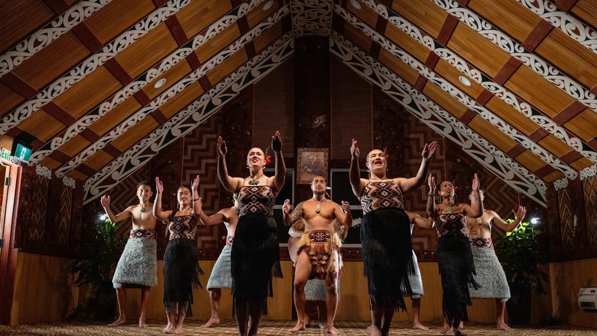 Māori cultural group performing waiata and haka inside a traditional carved wharenui meeting house in Rotorua