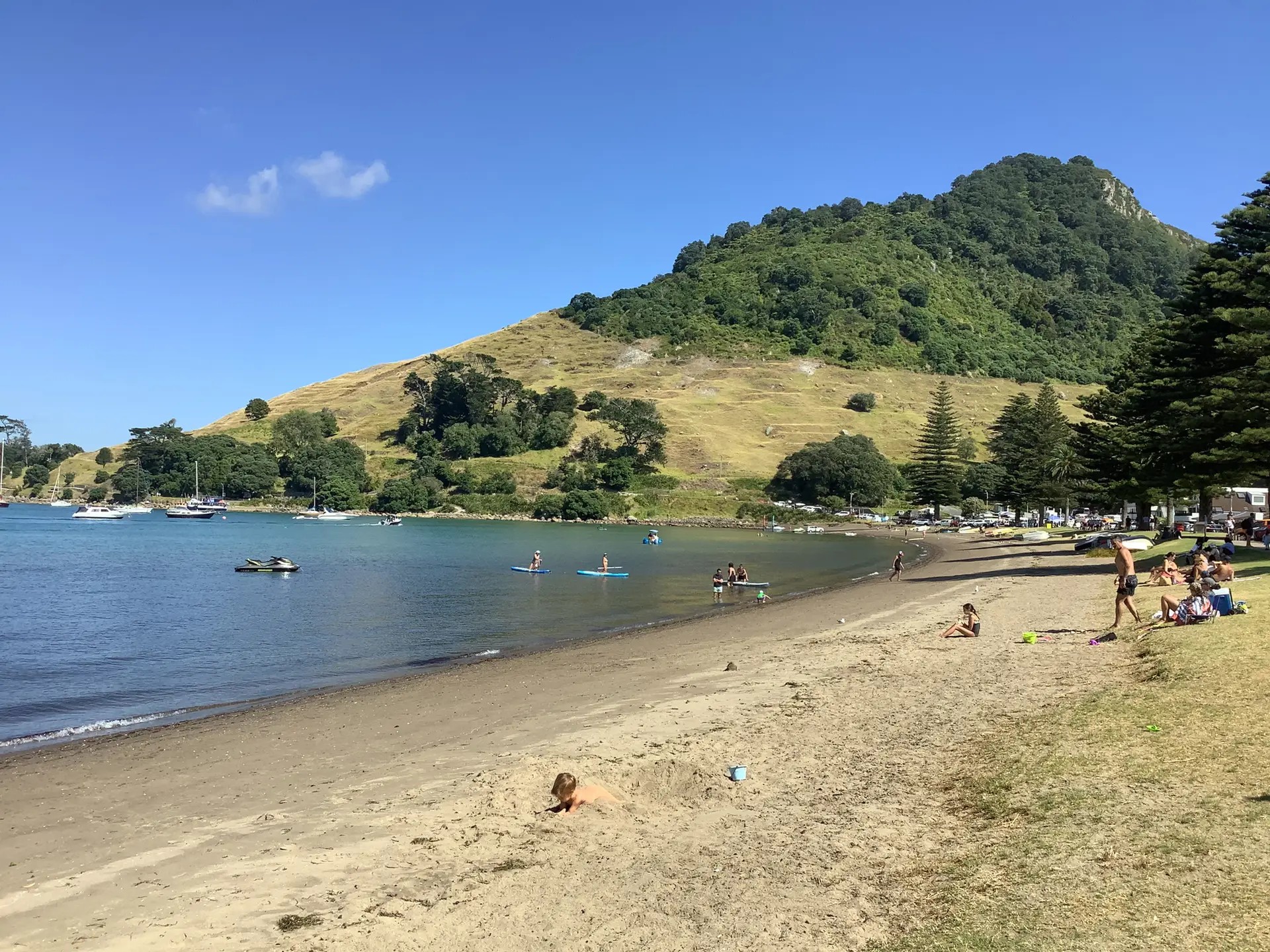 People playing in the sand and water of Pilot Bay Beach in front of Mount Maunganui.