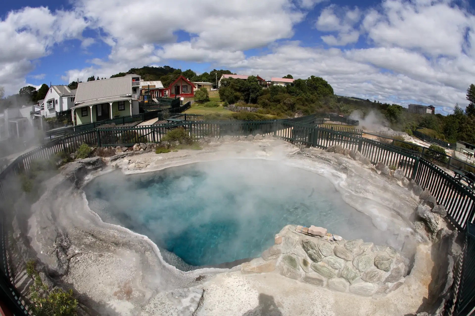 Steam vents coming out of a large, fenced geothermal pool in Whakarewarewa Village.