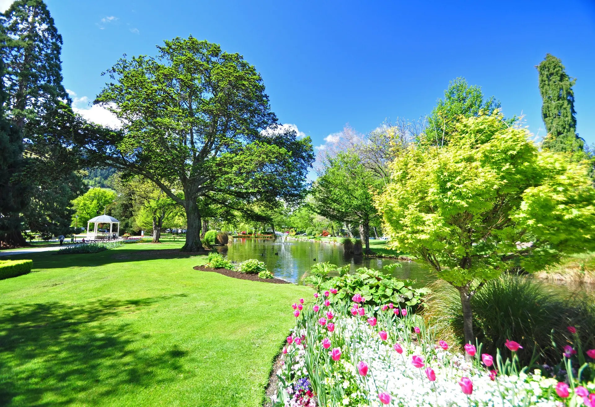 Park with a gazebo, river,trees, and flower garden on a sunny day.