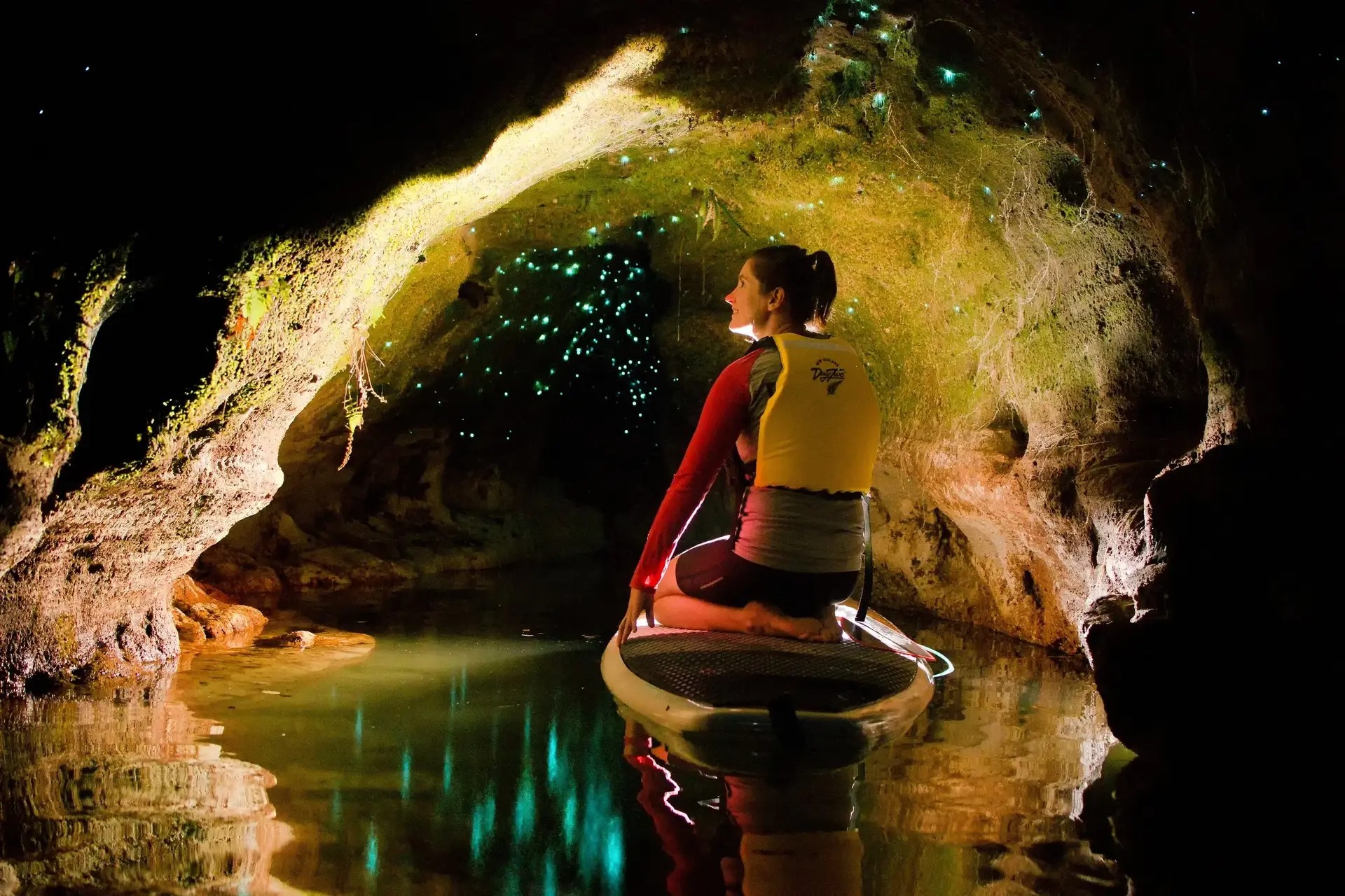 Solo paddleboarder exploring a dark cave with glowworms