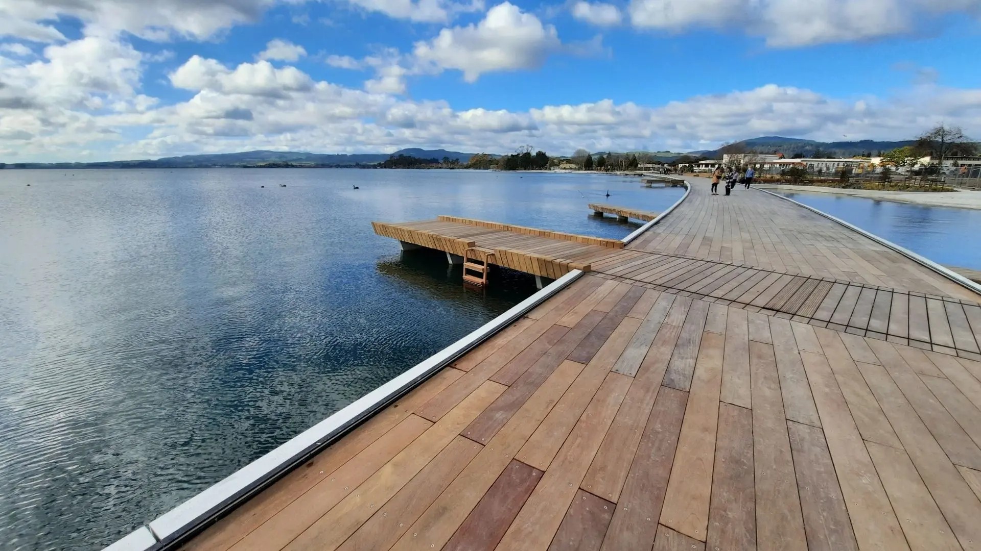 A large, contemporary wooden boardwalk curving around the perimeter of Lake Rotorua.