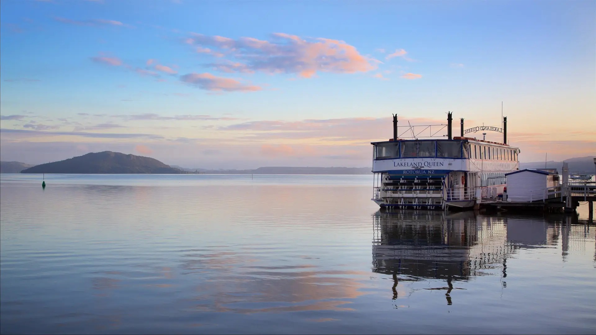 The Lakeland Queen historical cruise ship by the dock on Lake Rotorua near sunset.