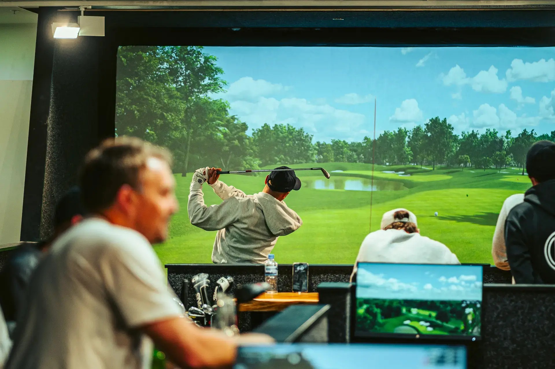 A man swinging in front of a golfing simulator screen.