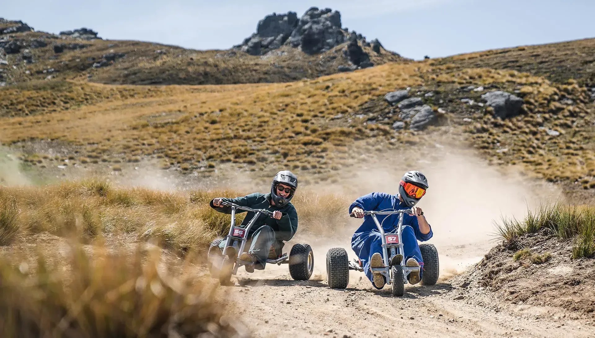 Two people race down a track on mountain carts.