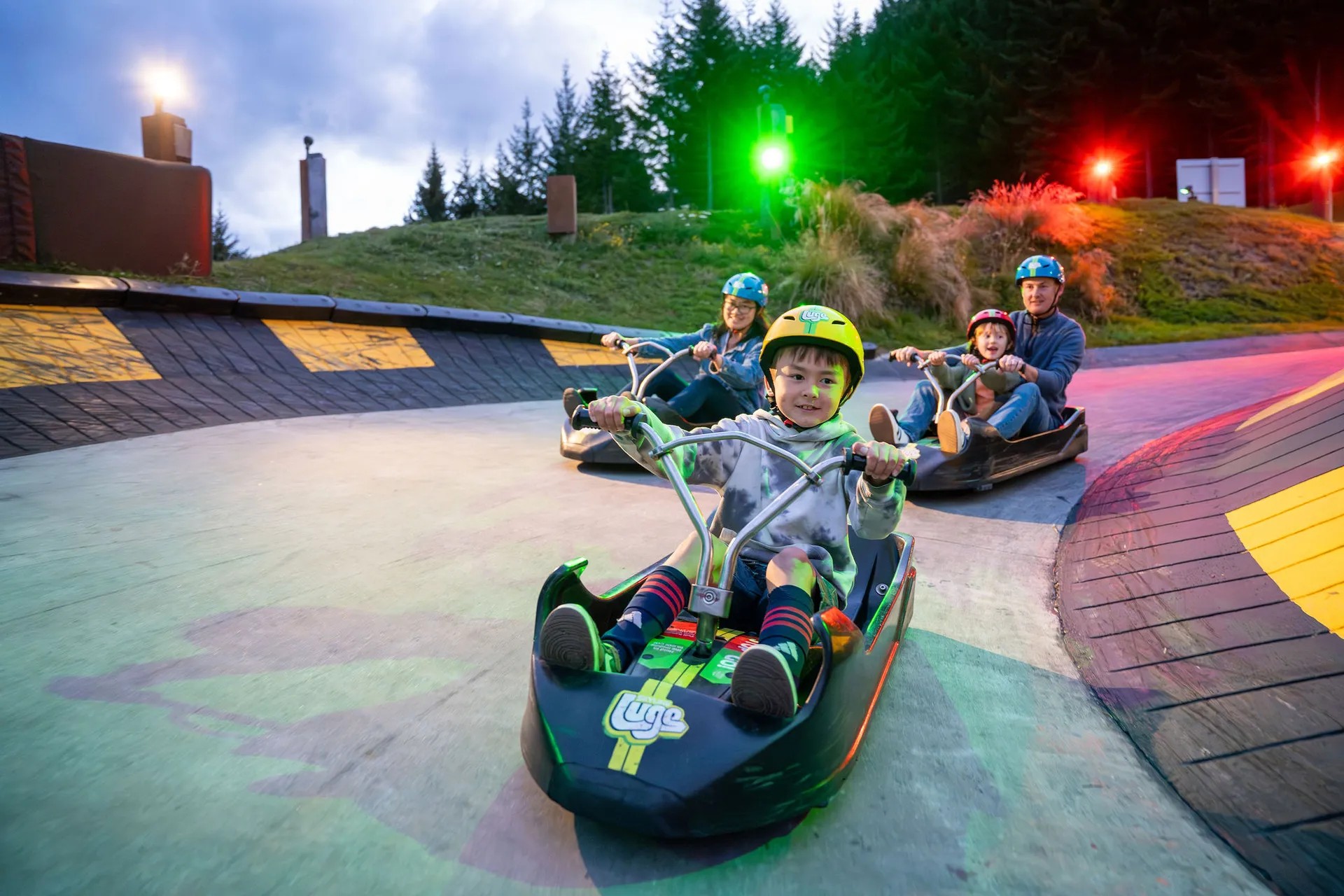 Family riding luge karts around the corner of a track.