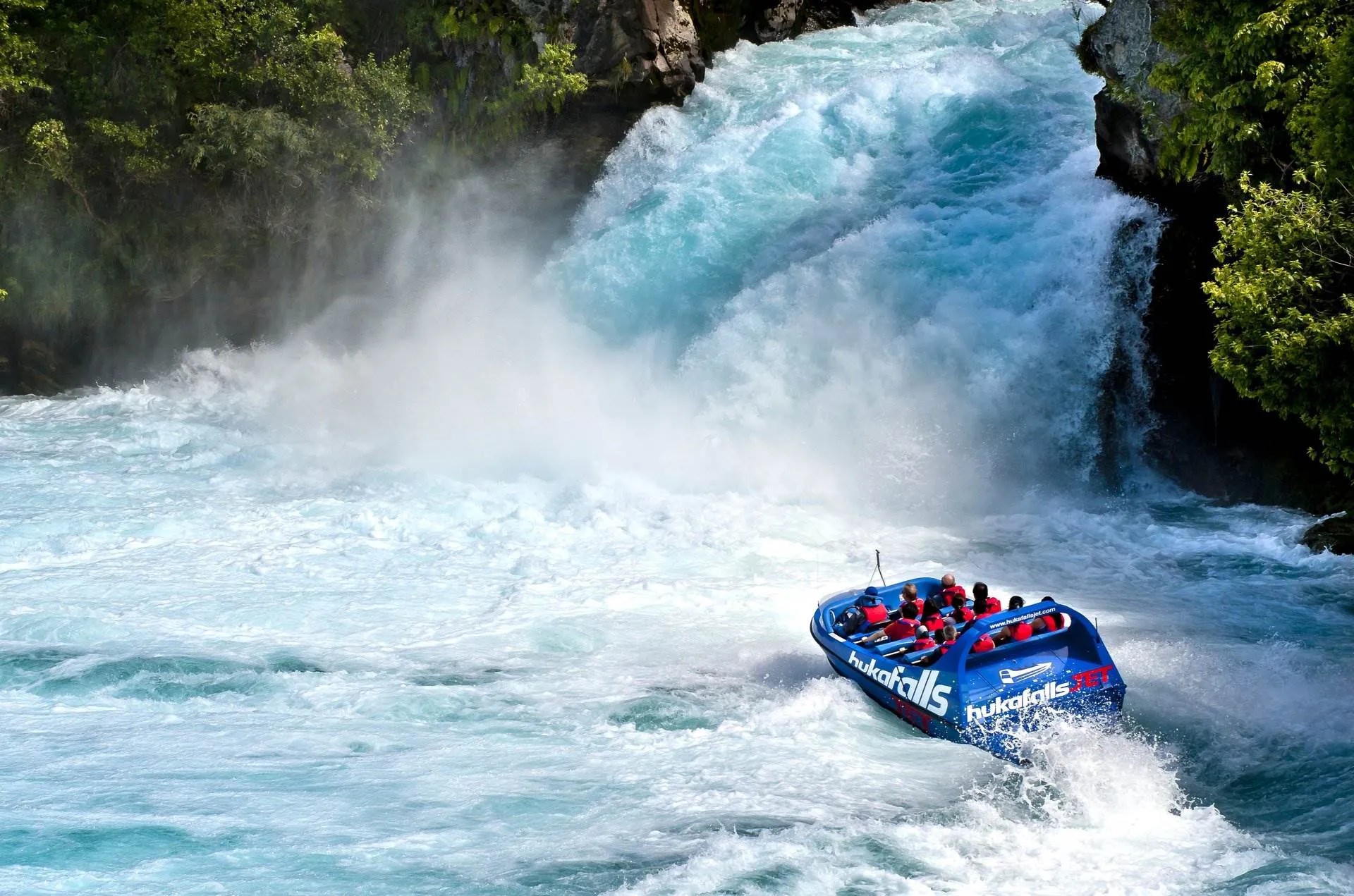 Blue jet boat approaching the gushing Huka Falls waterfall.