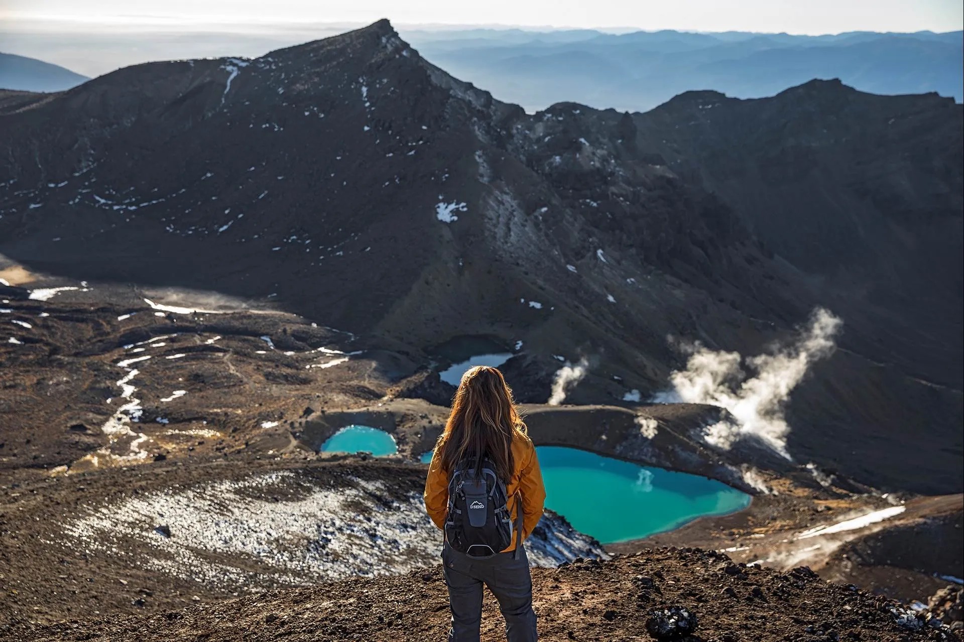 Woman looks at the Tongariro alpine range and turquoise lakes below.