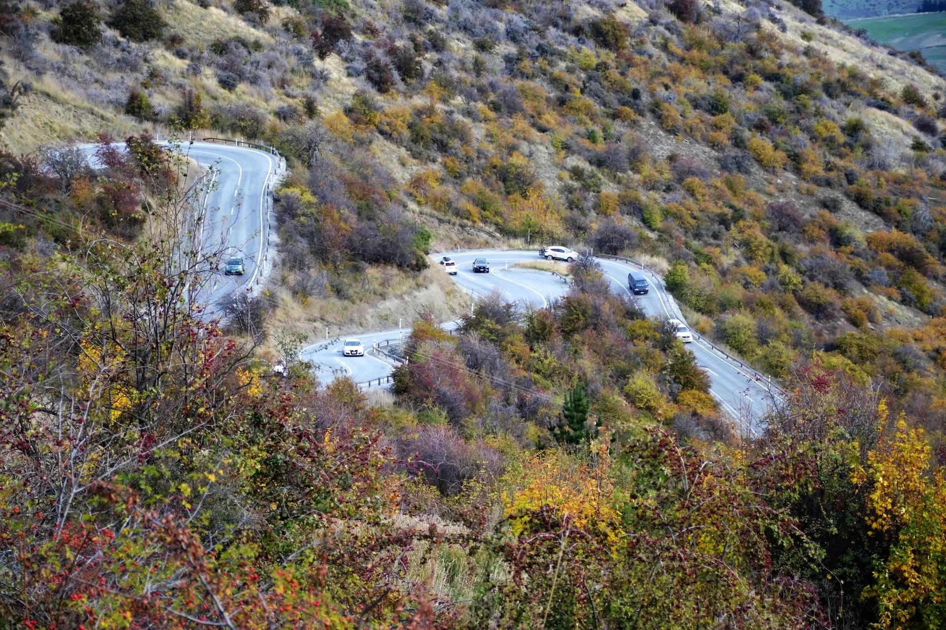 Crown Range Road Arrow Junction. Cars driving along a path zig-zagging up a mountain range.
