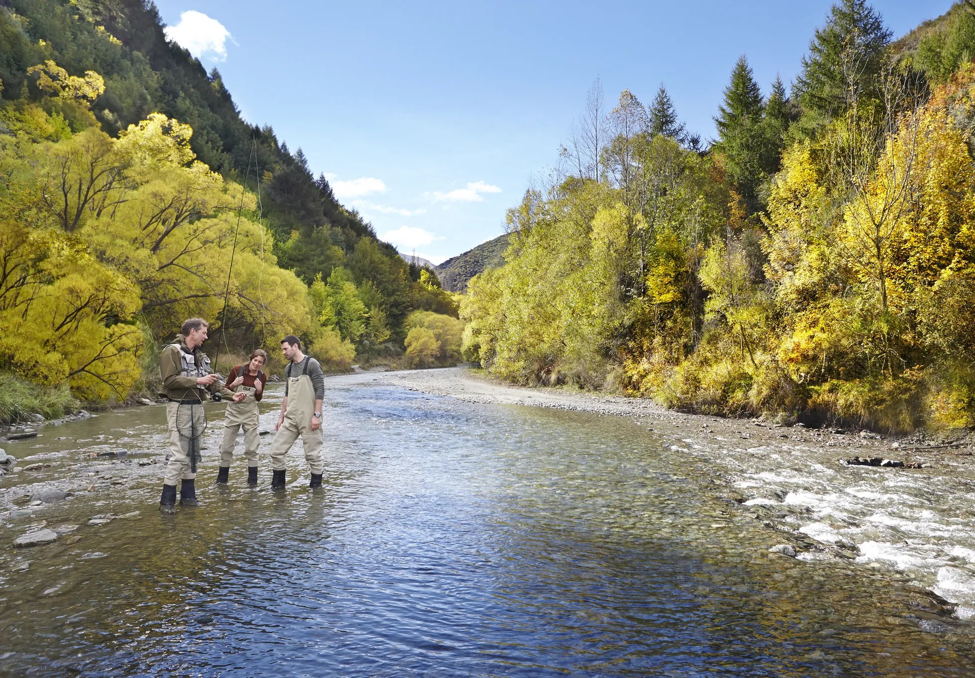 Three people fishing in a shallow river.