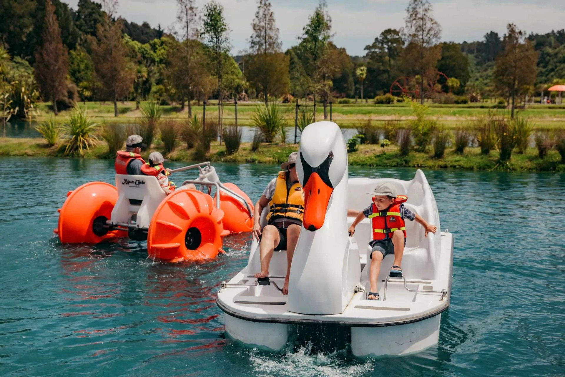 Family rides a swan pedal boat in a pond.