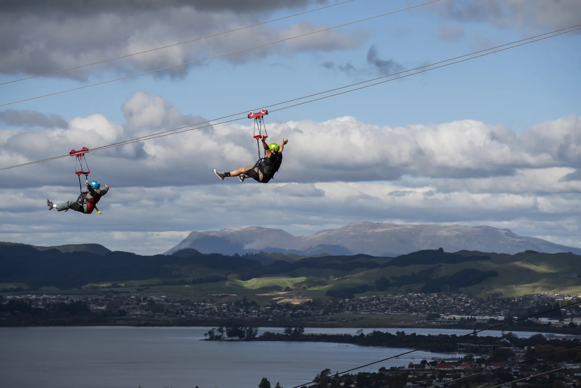 Two people excitedly riding a zipline with views of Lake Rotorua below.
