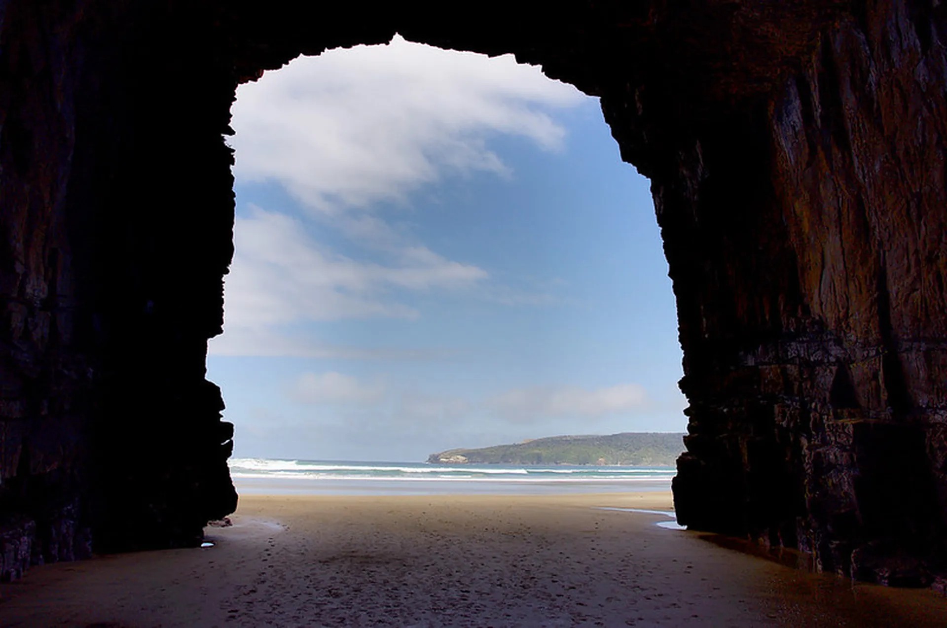 The view inside a cave with a large mouth, looking out onto a beach