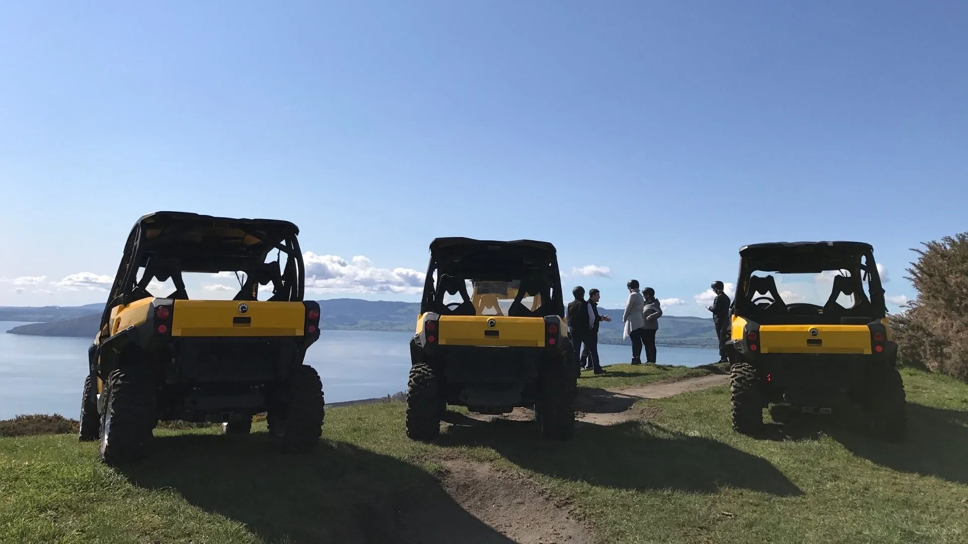 Three yellow 4WD buggies overlook Lake Rotorua from a cliff