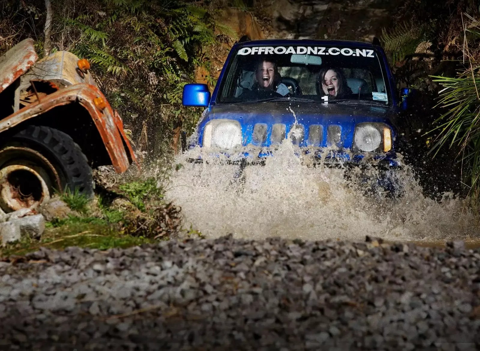 Two people in a 4WD car, driving into a muddy pond in a forest